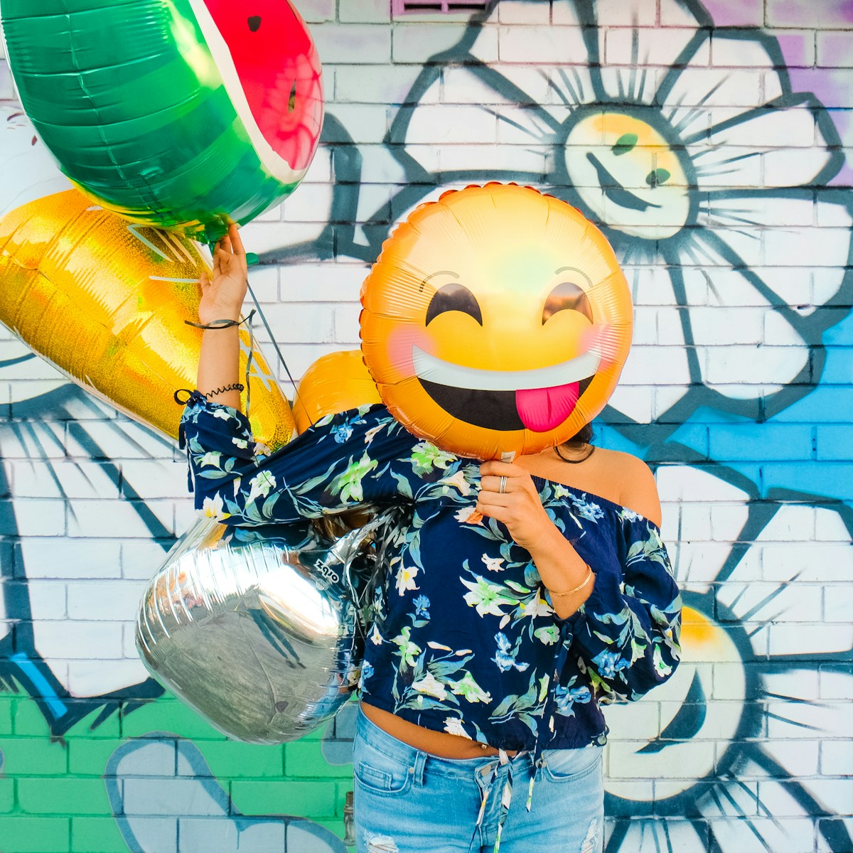 woman holding balloons. An emoji smiling face balloon is covering her face